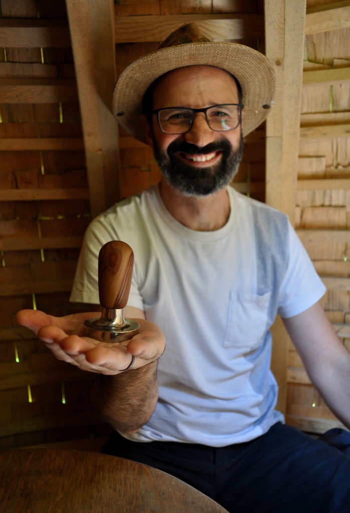 A photograph of me holding out a tamper with olive wood handle towards the viewer.